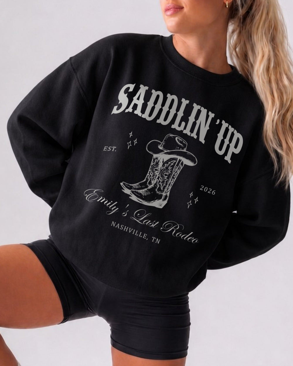 Bride and bridesmaid matching western bachelorette sweatshirts with vintage serif typography and saddlin up theme. Personalized with bride name, party destination, and year for the full crew.