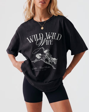 Bride and bridesmaids in matching Wild Wild Wife western tees for a rodeo bachelorette party. Vintage cowgirl illustration with script lettering for the whole bridal crew.