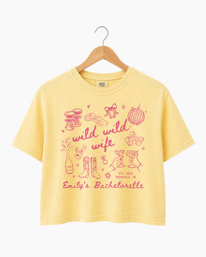 Personalized bachelorette crop top with bride name, date, and city on a Wild Wild Wife doodle design. Playful script lettering and line-art icons for the whole bachelorette crew.