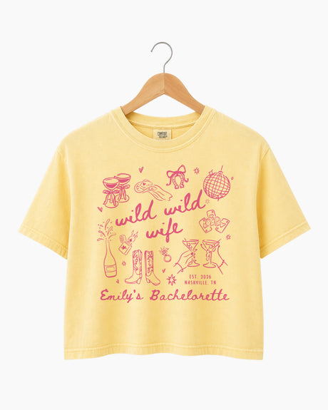 Personalized bachelorette crop top with bride name, date, and city on a Wild Wild Wife doodle design. Playful script lettering and line-art icons for the whole bachelorette crew.