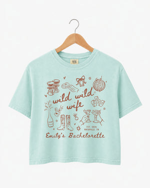 Bride and bridesmaids matching boxy crop tees for a Wild Wild Wife bachelorette weekend. Personalized with bride name, EST year, and destination city for the full crew.