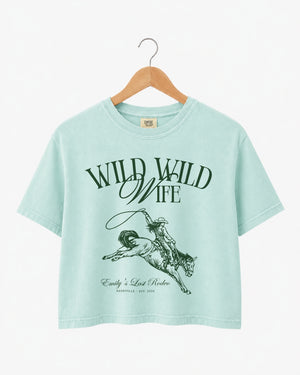 Gift idea for the bride: Wild Wild Wife cowgirl bachelorette crop top with vintage western art. Personalized with bride name, destination, and year for the whole crew.