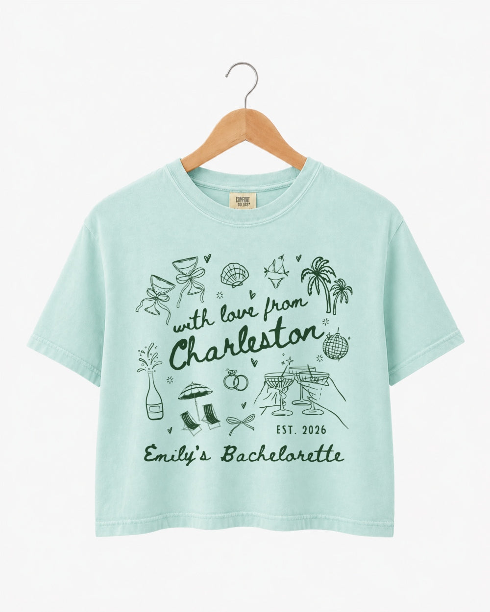 Gift idea for the bride-to-be: Charleston bachelorette crop top with hand-drawn doodle script and playful icons. Personalized with bride name, destination city, and EST year for the whole crew.