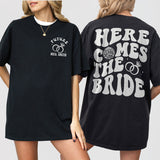Retro disco-inspired black cotton shirt with 'Here Comes The Bride' design, perfect for bachelorette parties or bridesmaid gifts
