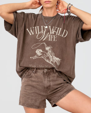 Bride and bridesmaids in matching Wild Wild Wife western tees for a rodeo bachelorette party. Vintage script lettering and cowgirl illustration for the whole bridal crew.