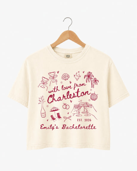 Bachelorette weekend crop top with hand-drawn doodle script and playful icons for the Charleston bride and her crew. Personalized with bride name, destination city, and year.
