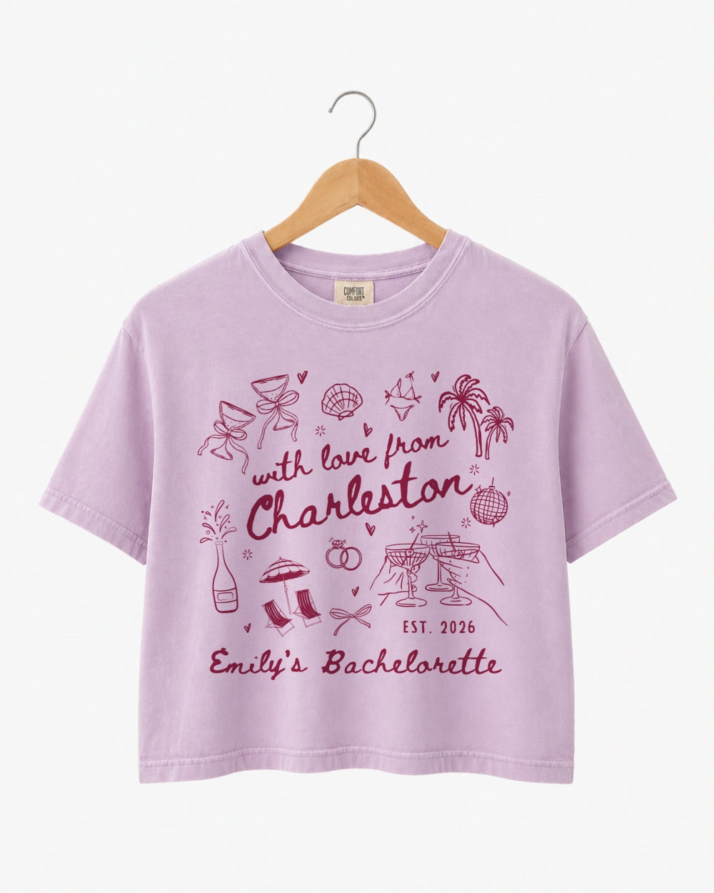 Bride and bridesmaids matching crop tops for a Charleston bachelorette weekend. Hand-drawn doodle script with playful icons, personalized with bride name, destination city, and EST year.