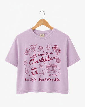 Bride and bridesmaids matching crop tops for a Charleston bachelorette weekend. Hand-drawn doodle script with playful icons, personalized with bride name, destination city, and EST year.