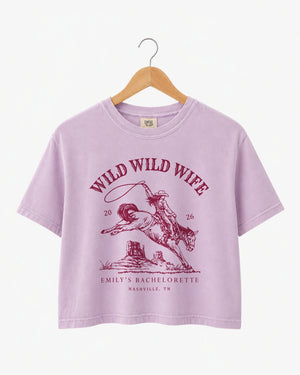 Bride and bridesmaid crop tops for a Wild Wild Wife bachelorette weekend with vintage western rodeo art. Personalize with bride name, year, and destination city for the full crew.