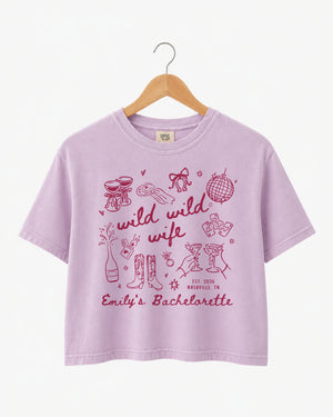 Maid-of-honor gift idea: Wild Wild Wife bachelorette crop top with playful doodle art and script lettering. Personalized with bride name, weekend date, and destination city for the whole crew.