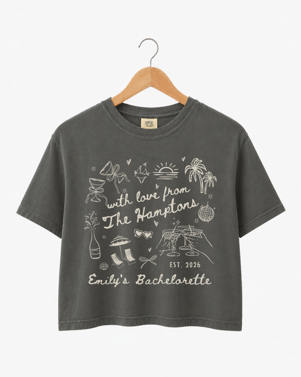 Cropped bachelorette top with Hamptons-theme illustrated doodle art and script lettering. Personalized with bride name, year, and destination for the full bachelorette crew.