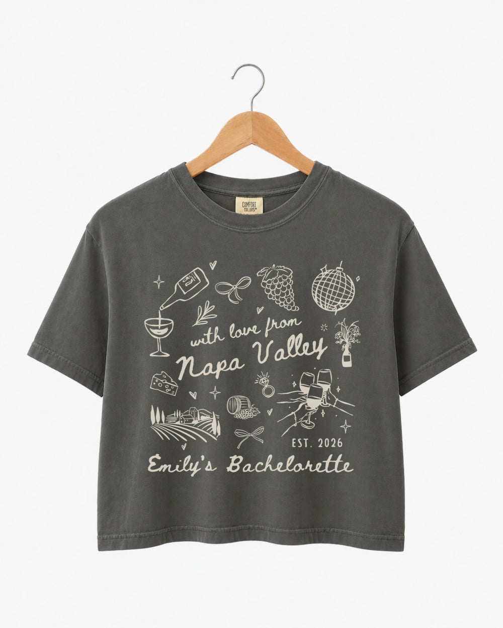 Cropped bachelorette tee with whimsical Napa Valley line-art doodles and script typography. Personalized with bride name, weekend date, and destination for the full bridal crew.