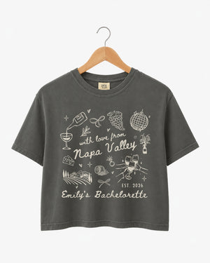 Cropped bachelorette tee with whimsical Napa Valley line-art doodles and script typography. Personalized with bride name, weekend date, and destination for the full bridal crew.