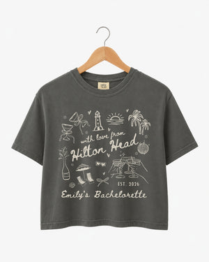 Cropped bachelorette tee with playful line-art doodles and hand-drawn script, personalized with bride name, destination city, and EST year for the whole Hilton Head crew.