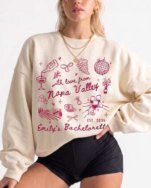 Personalized Napa Valley bachelorette sweatshirt with bride name, year, and winery destination in whimsical script and line-art doodles. Custom matching set for the whole bridal crew.