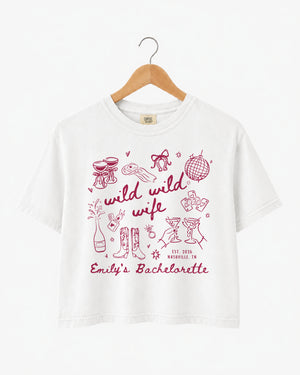 Boxy cropped bachelorette tee with playful doodle art and Wild Wild Wife script lettering for the bride and her crew. Personalize with bride name, date, and destination city.